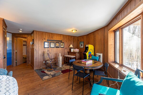 A cozy room with wooden walls, a round dining table, and a window with a view of trees. - Vista 360 - Roundhouse with views, AC, 1mi from Beech Ski (Beech Mountain)