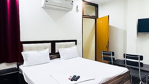 Ein Hotelzimmer mit einem Bett, einem Schreibtisch, einem Sessel, einer Klimaanlage, einem Deckenventilator und einem Fernseher.