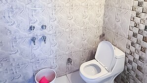 Ein Badezimmer mit gemusterten Fliesen, einer Toilette, einem Waschbecken und einem Eimer.