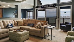 Een moderne woonkamer met een groot raam met uitzicht op Lake Charlevoix, een beige modulaire bank, een klein bijzettafeltje en zicht op het water.