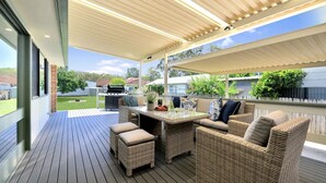 A covered outdoor patio with wicker furniture, a grill, and a view of the backyard. - Plumeria – 350m to beach track, pet friendly (Callala Beach)