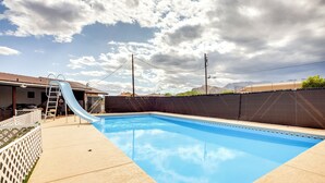 Una piscina con tobogán, rodeada por una valla y una escalera.