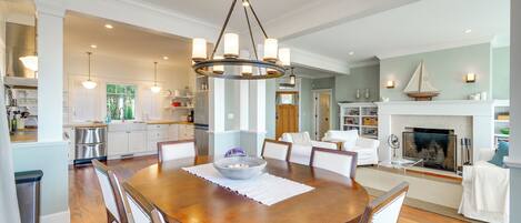 A spacious dining area with a wooden table, white upholstered chairs, and a central chandelier.