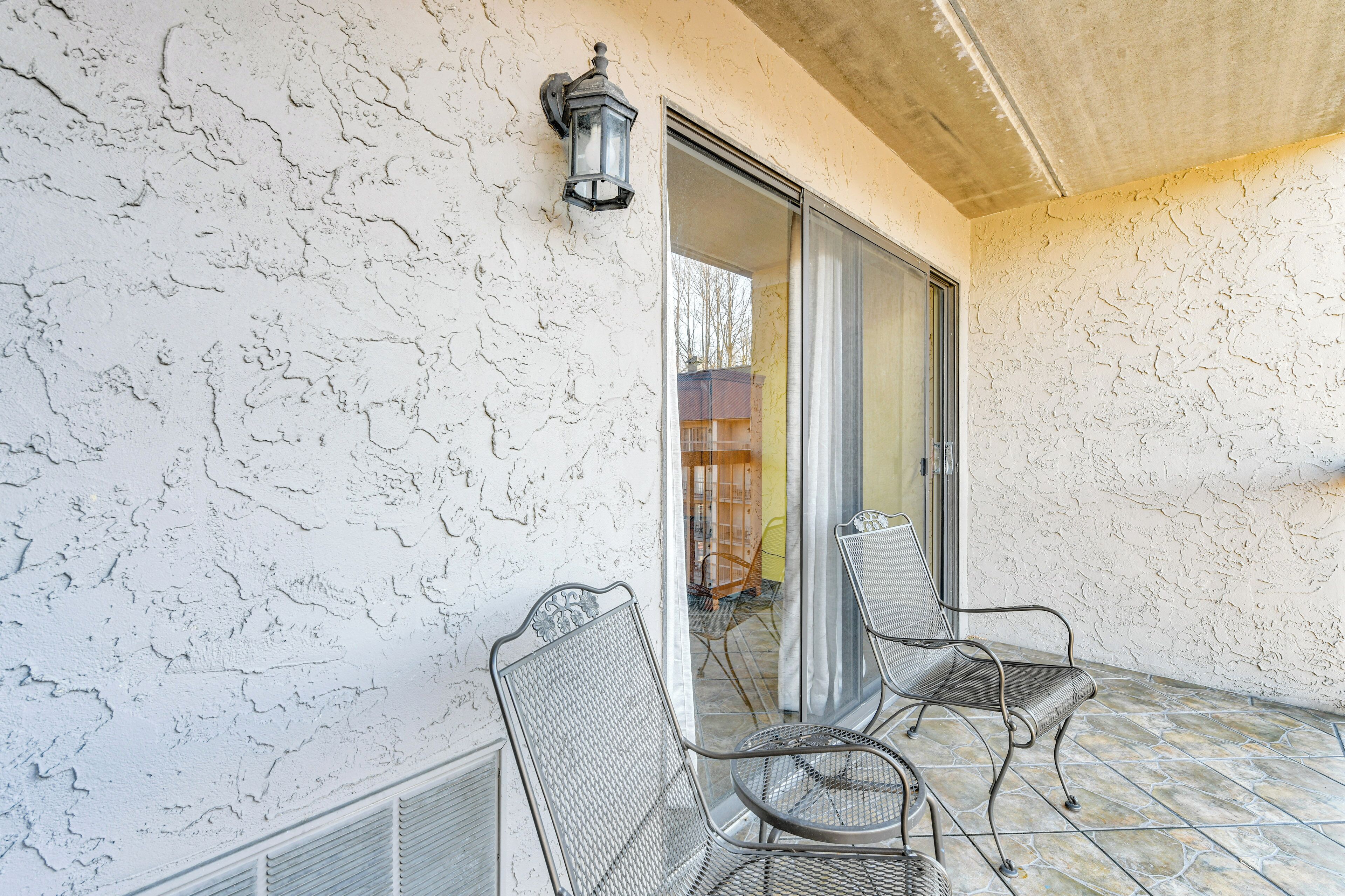 Eine überdachte Terrasse mit strukturierten Wänden, einem Metallstuhl, einem Metalltisch und einer Schiebetür zu einem Innenraum.