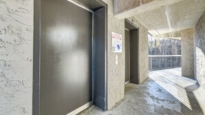 Un pasillo con la puerta de un ascensor cerrado, un cartel que indica su uso y vistas a un área de balcón exterior.