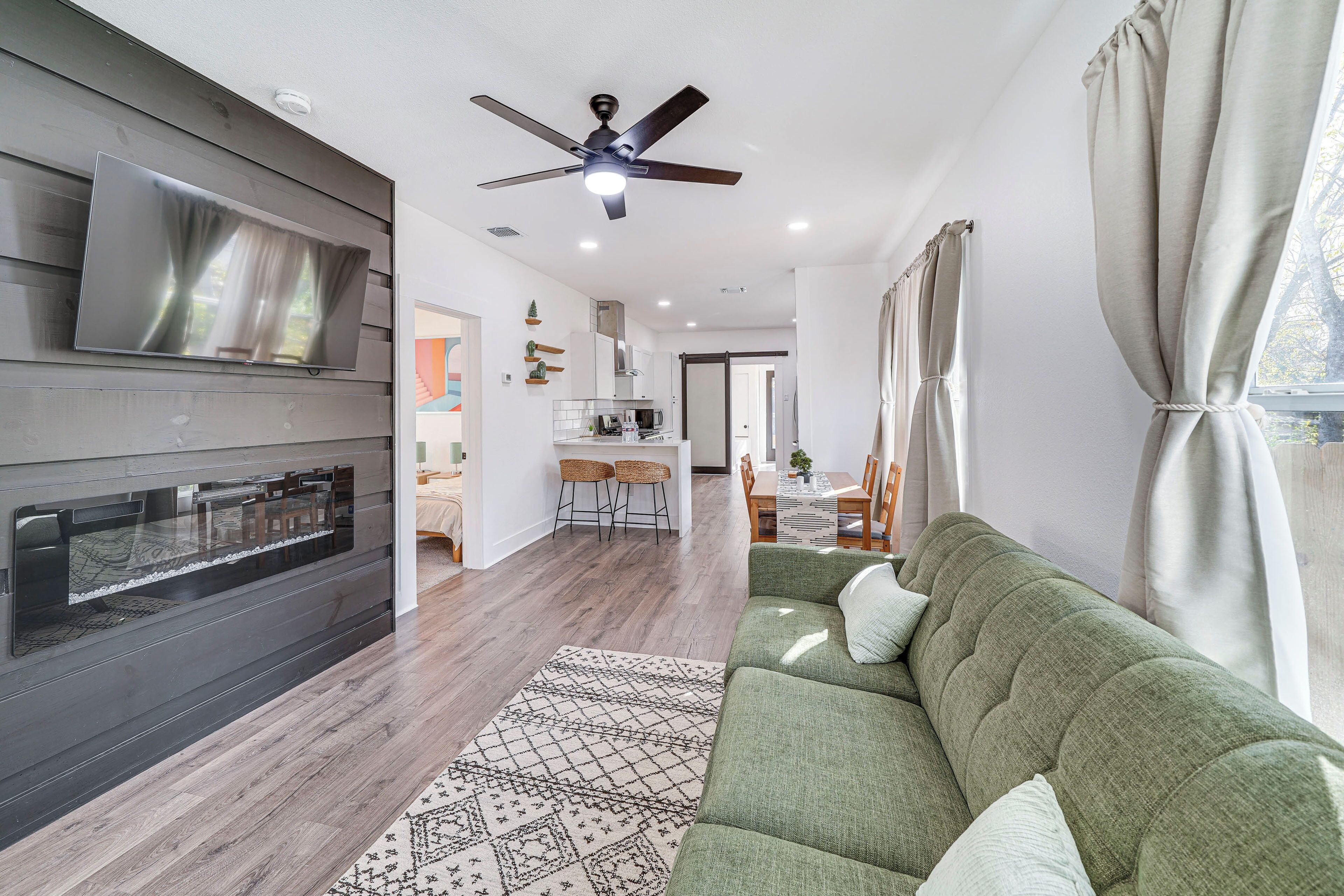 A modern living room with a flat-screen TV, a ceiling fan, a green sofa, and a patterned rug.