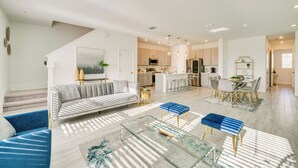 A spacious living area with a sofa, coffee table, and ottoman, a kitchen in the background, and a staircase leading to another level. - Stylish Four Corners Townhome w/ Resort Amenities (Davenport)