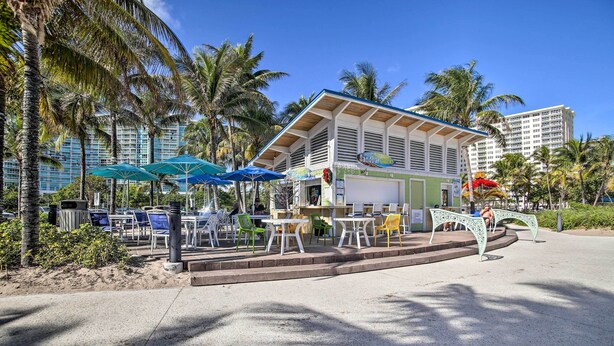 Un restaurante frente a la playa con terraza, palmeras y vista al océano.
