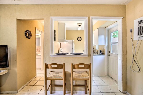 A hallway with two wooden chairs, a clock, and a window with a view of a kitchen.