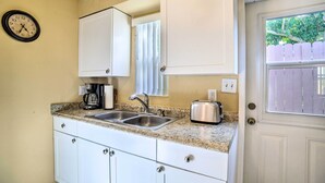 Una cocina con armarios blancos, un lavamanos doble, un tostador y un reloj en la pared.