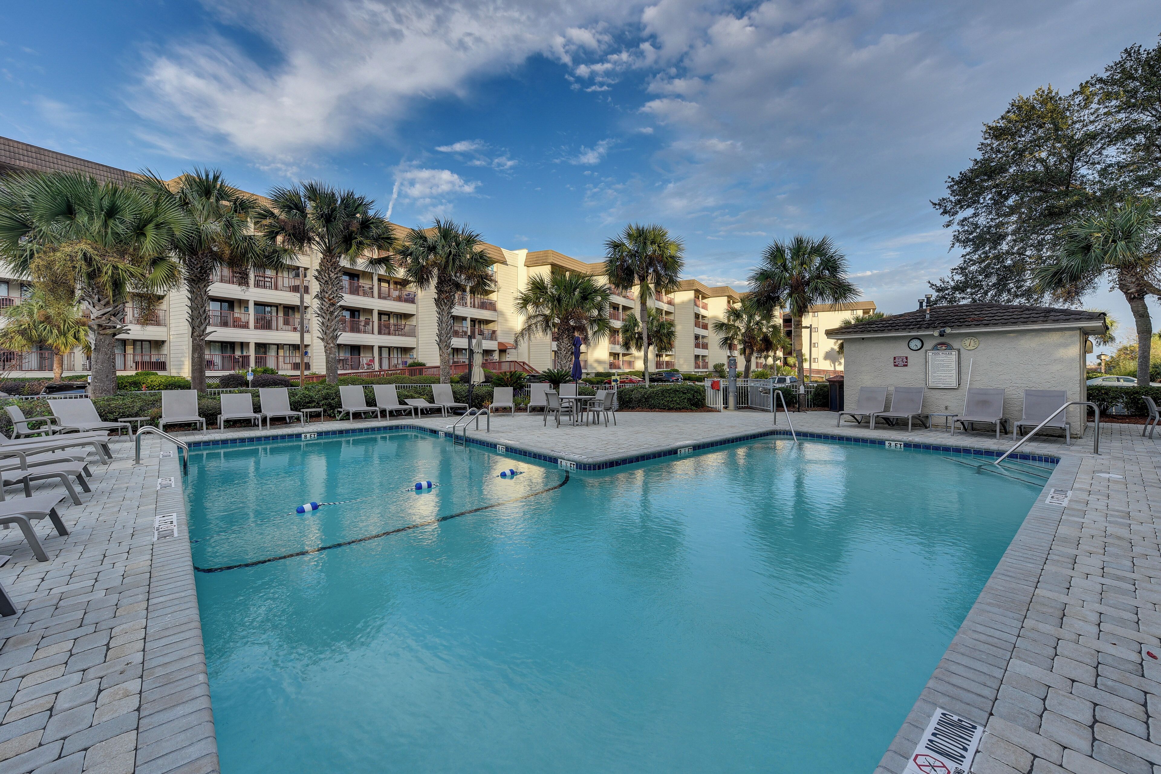 A swimming pool with lounge chairs and palm trees, surrounded by multi-story buildings.