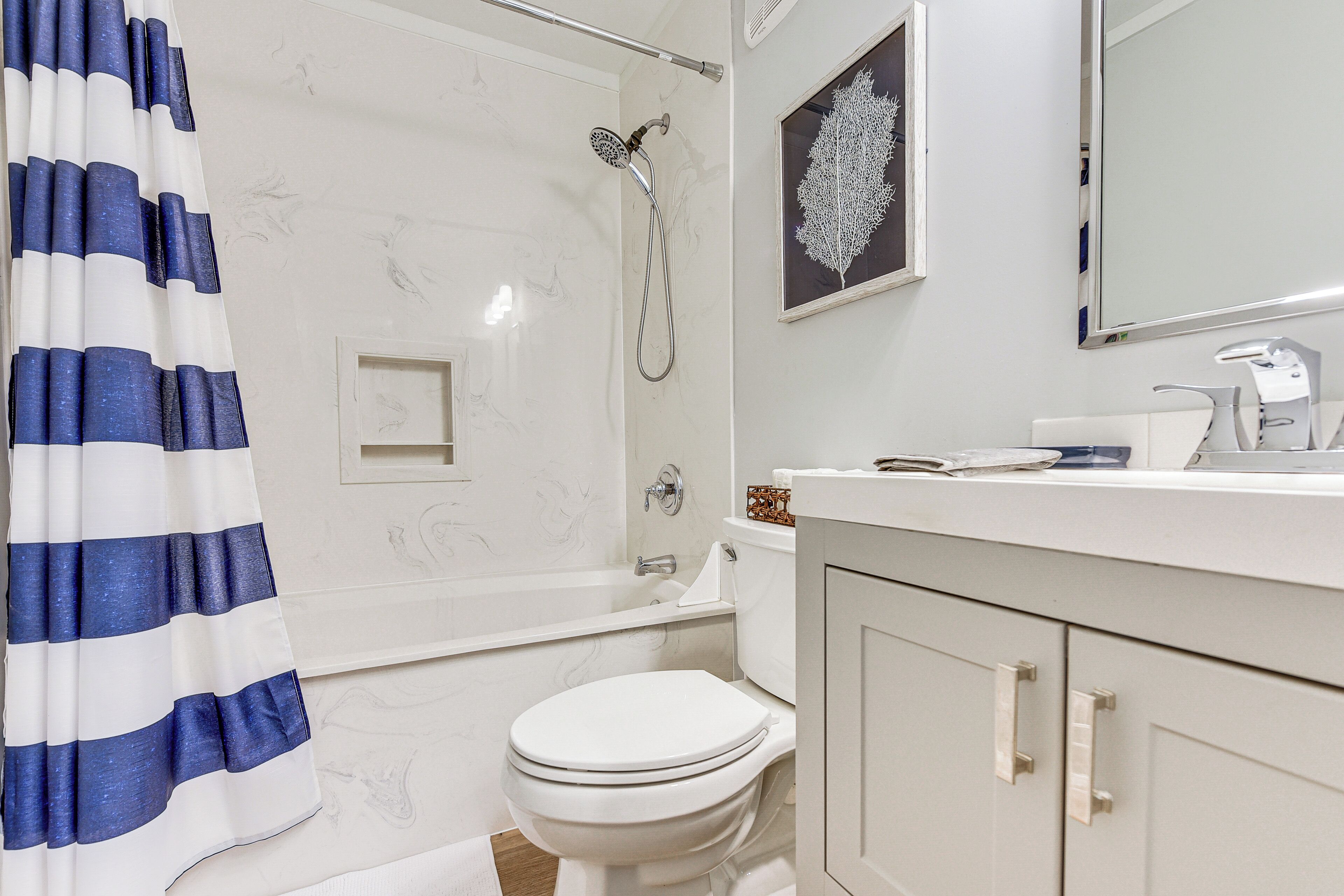 Et badeværelse med brusebad, toilet og vask med et spejl over.