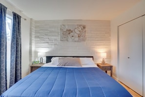 A bedroom with a large bed, a white brick wall, a decorative flower painting, a nightstand with a lamp, and a wardrobe. - Wildcats Welcome! Mtn-view Condo 7 Mi to U of A (Tucson)