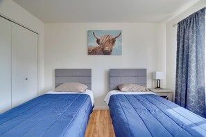 Une chambre d’hôtel avec deux lits, un tableau représentant un taureau, une table de chevet et une fenêtre avec des rideaux.