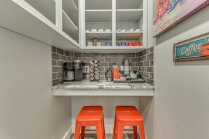 Una cucina con un piano di lavoro bianco, una macchina da caffè e uno scaffale con tazze e mug.