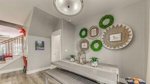 Un interior moderno con una escalera, un banco y decoraciones en la pared, incluyendo coronas y cuadros.