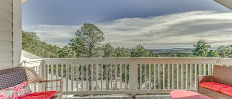 A covered deck with wicker furniture and a table, overlooking a scenic landscape.