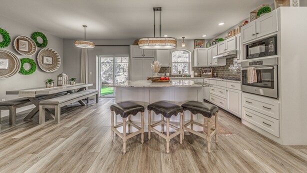 Una cocina moderna con armarios blancos, una isla central, taburetes de bar y una mesa de comedor.