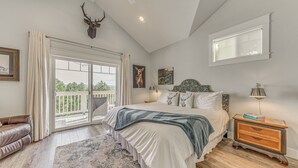 Un dormitorio con una cama grande, una mesita de noche, una ventana y una decoración de cabeza de venado montada en el techo.