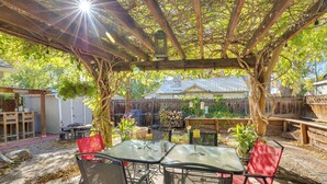 Un espace extérieur aménagé en terrasse, avec une pergola, des tables, des chaises et une clôture en bois en arrière-plan.