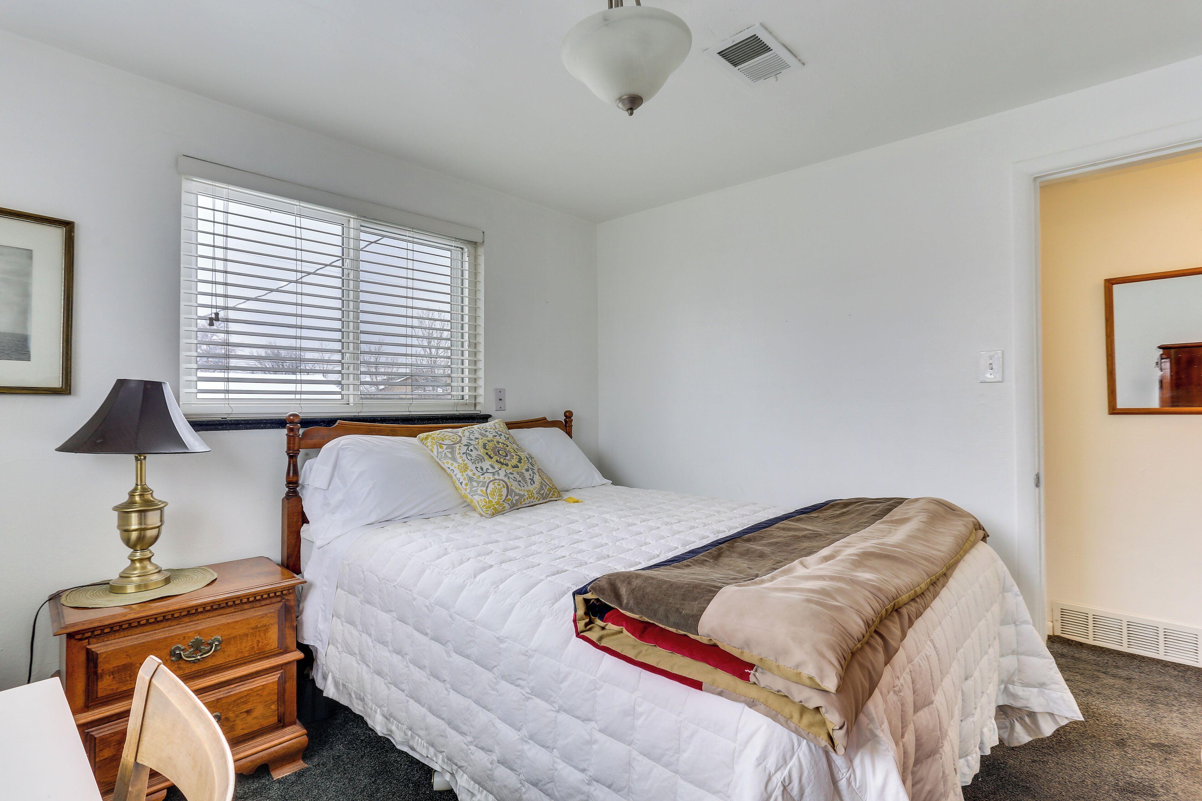 A bedroom with a bed, bedside table, lamp, and window.