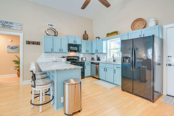 A modern kitchen with light blue cabinets, stainless steel appliances, and a central island with bar stools.