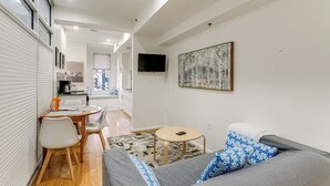 Un salon moderne avec un canapé gris, une petite table ronde et un téléviseur fixé au mur.