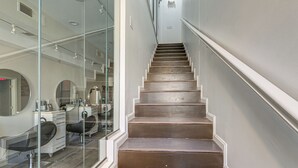 Un escalier menant à un salon aux murs de verre et à l’intérieur blanc.