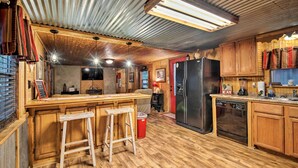 Una cocina rústica con armarios de madera, una barra con taburetes, un refrigerador y un lavavajillas.