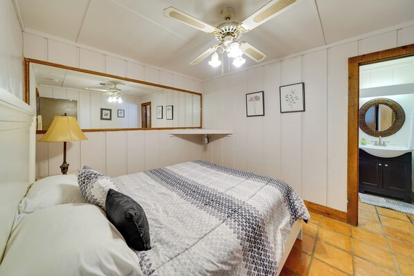 A bedroom with a bed, a ceiling fan, a mirror, and a bathroom visible through an open door.