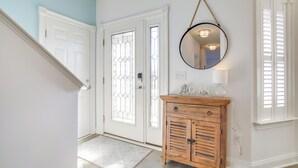 Un couloir avec une armoire en bois, un miroir et une porte à panneaux de verre.