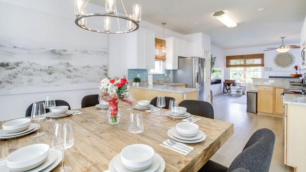 Une cuisine moderne avec des meubles blancs, une table à manger en bois pour six personnes et un lustre.
