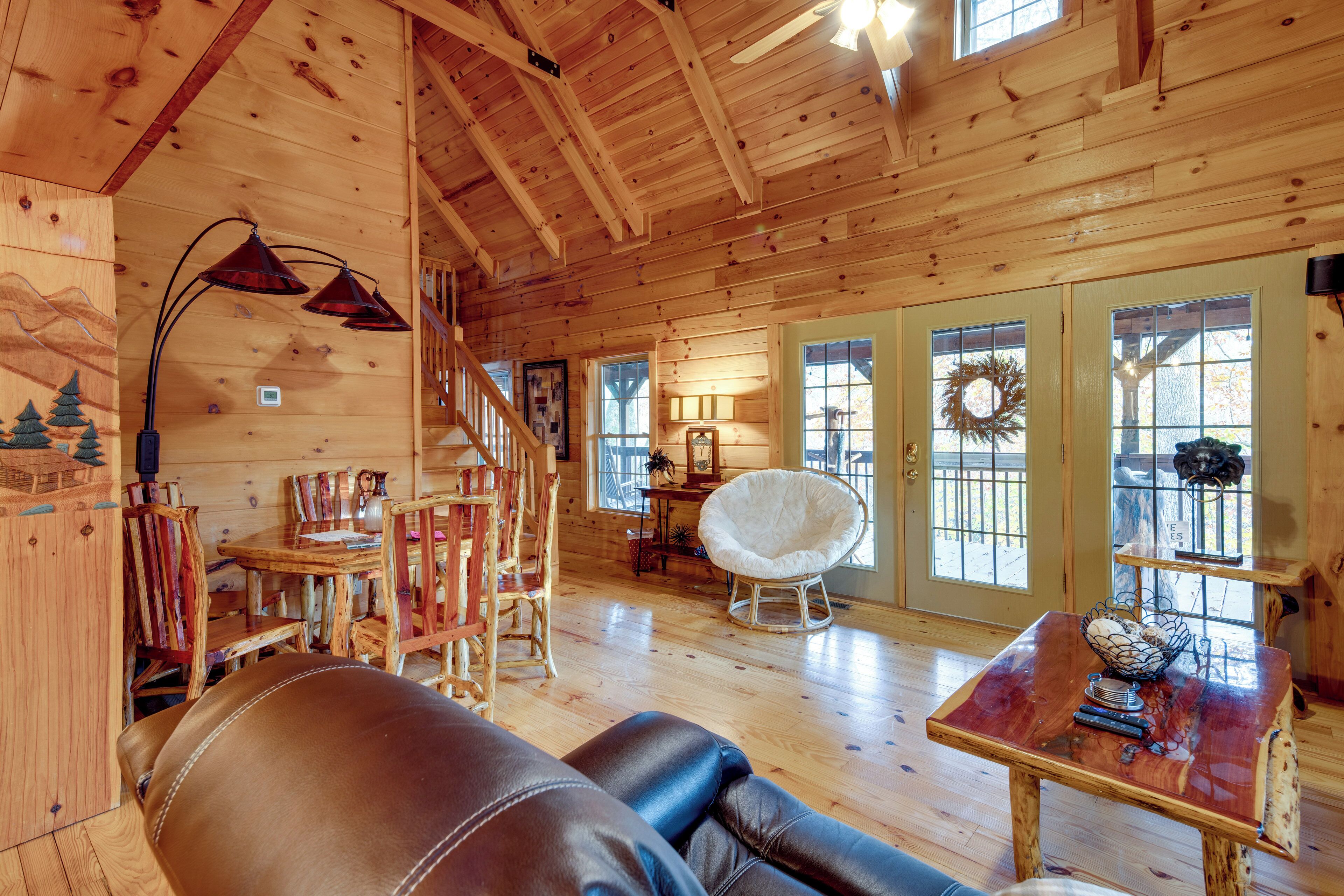 A wooden cabin interior with a leather couch, wooden dining table, and a staircase.