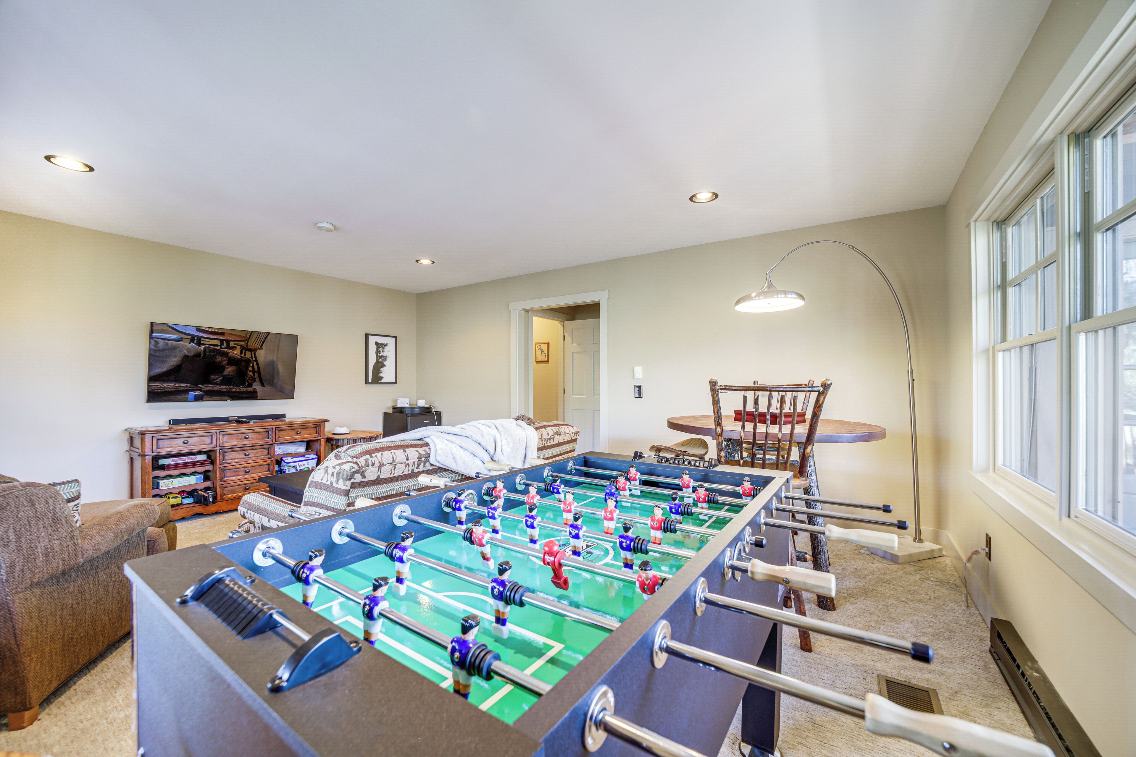 A living room with a foosball table, a television, and a dining area with chairs and a table.