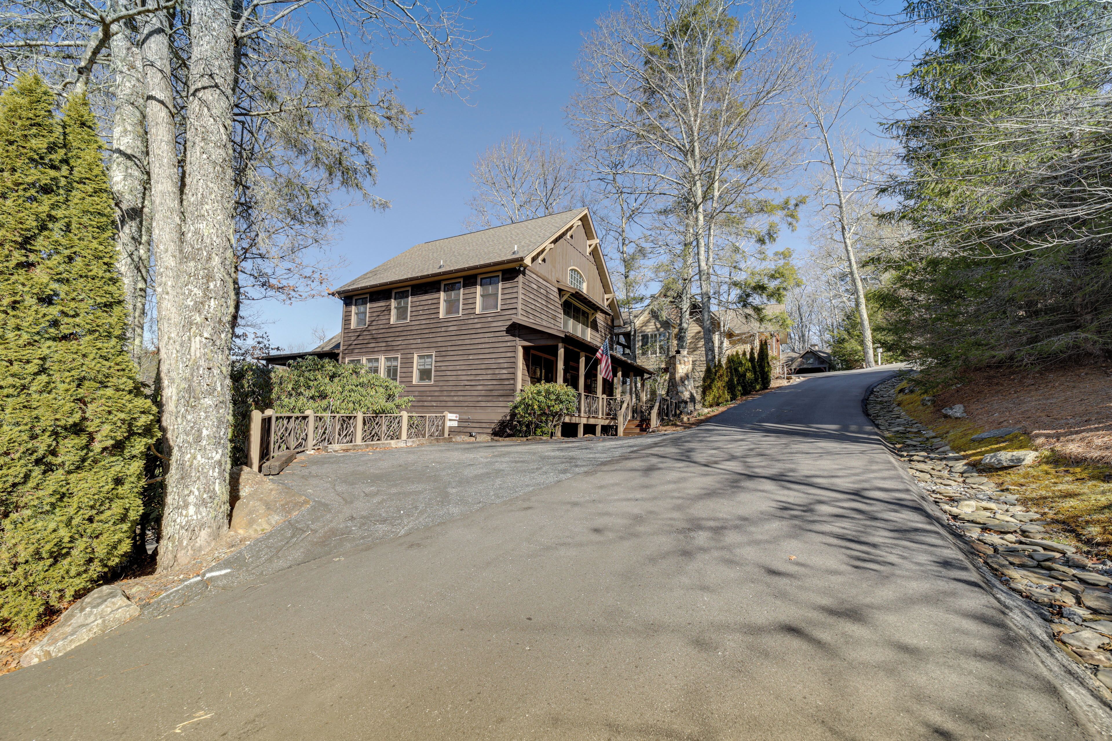 A two-story wooden house with a porch, a driveway, and a stone wall on one side.