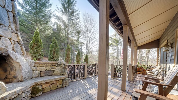 Una terraza de madera con escalones de piedra, mobiliario exterior y vistas a árboles.