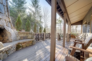 Una terraza de madera con escalones de piedra, mobiliario exterior y vistas a árboles.