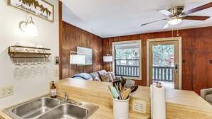 A kitchen with a double sink, wooden cabinets, a ceiling fan, and a window overlooking a deck. - Shuttle to the Resort! Rustic Angel Fire Condo (Angel Fire)