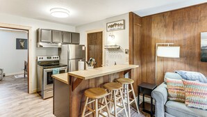 A kitchen with wooden cabinets, a stainless steel refrigerator, a stove, and a bar area with stools. - Shuttle to the Resort! Rustic Angel Fire Condo (Angel Fire)