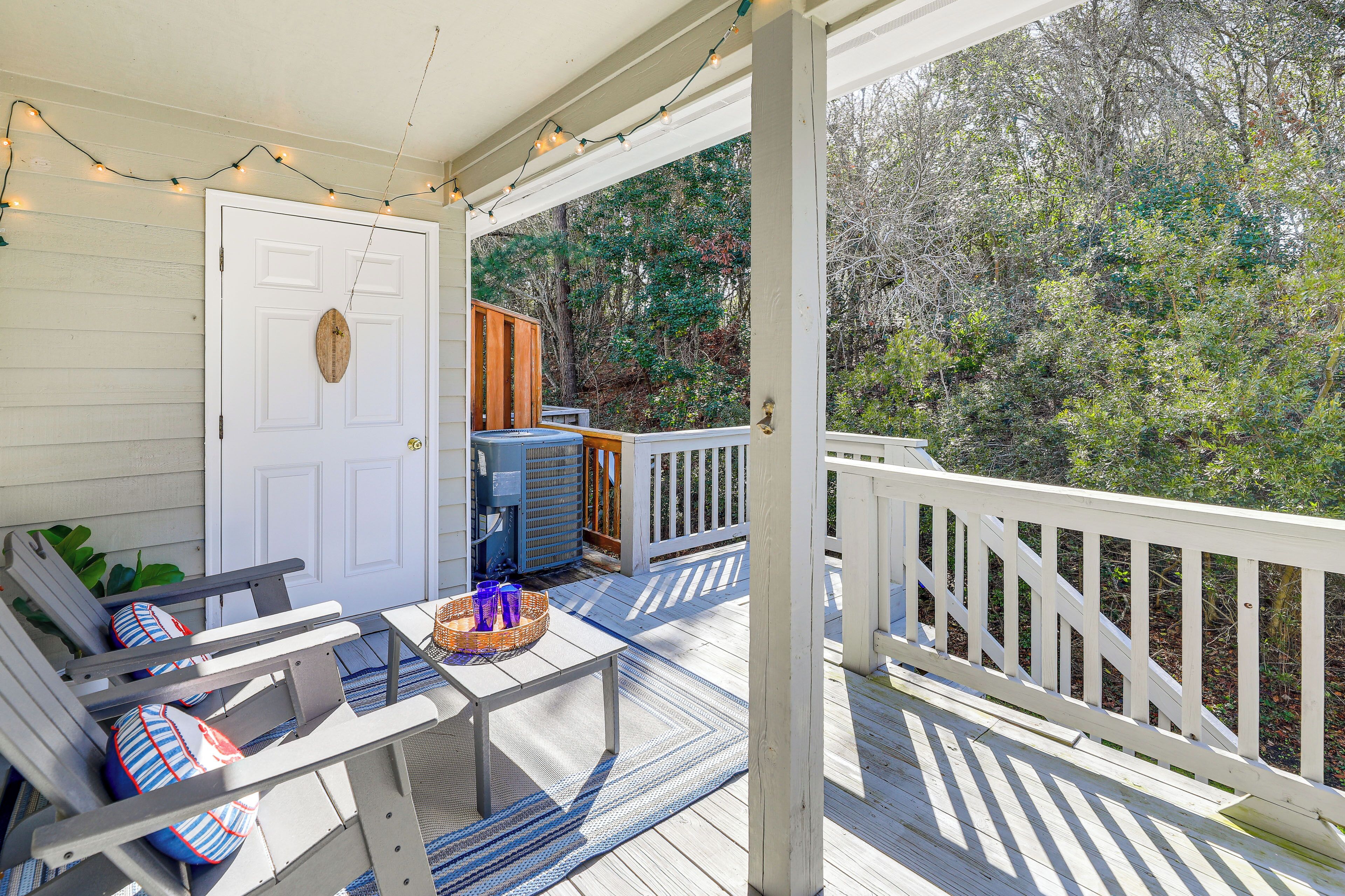 A covered porch with a white door, a table with chairs, and a view of trees.