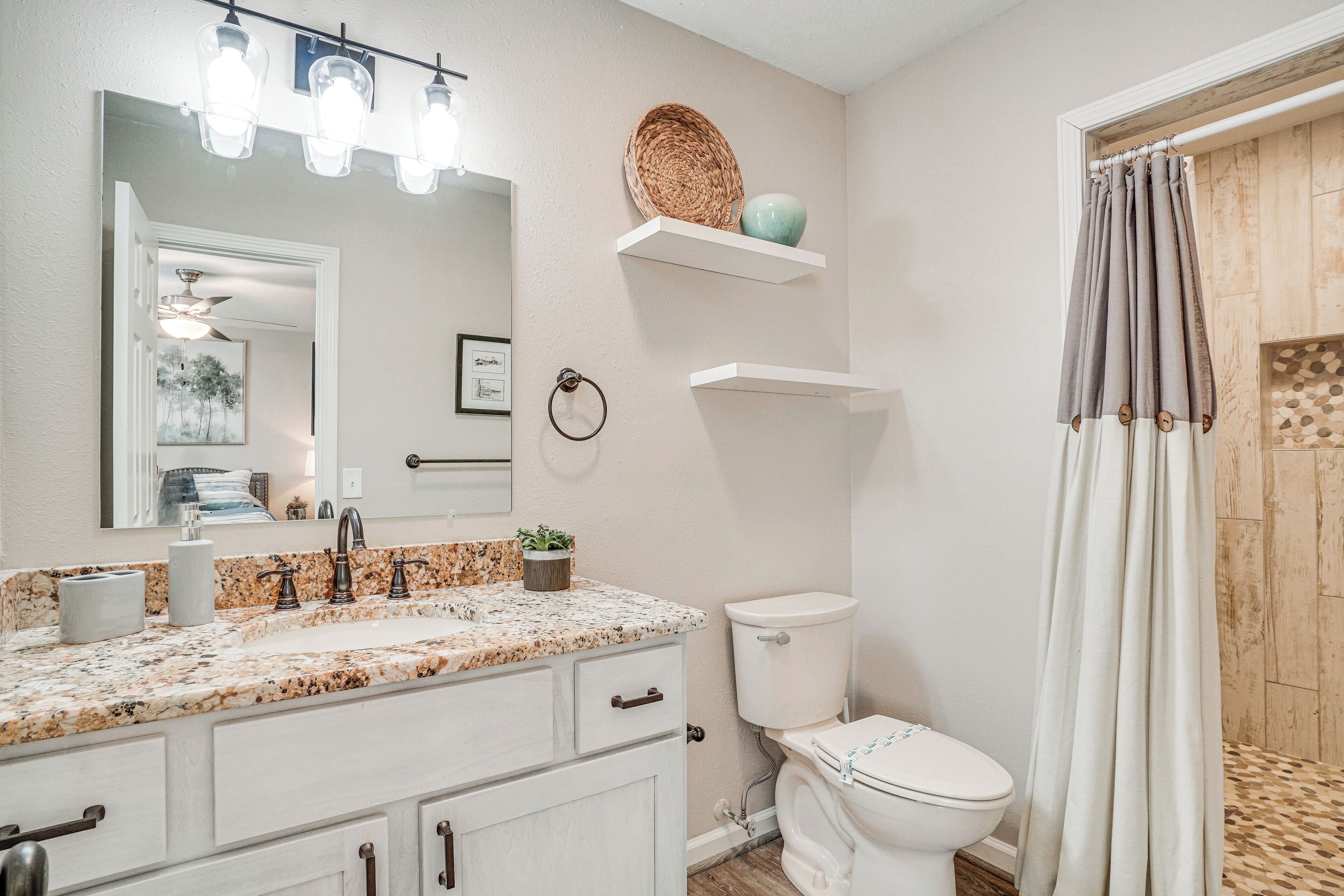 A bathroom with a white sink, a mirror, and a toilet. There are shelves above the toilet and a shower curtain.