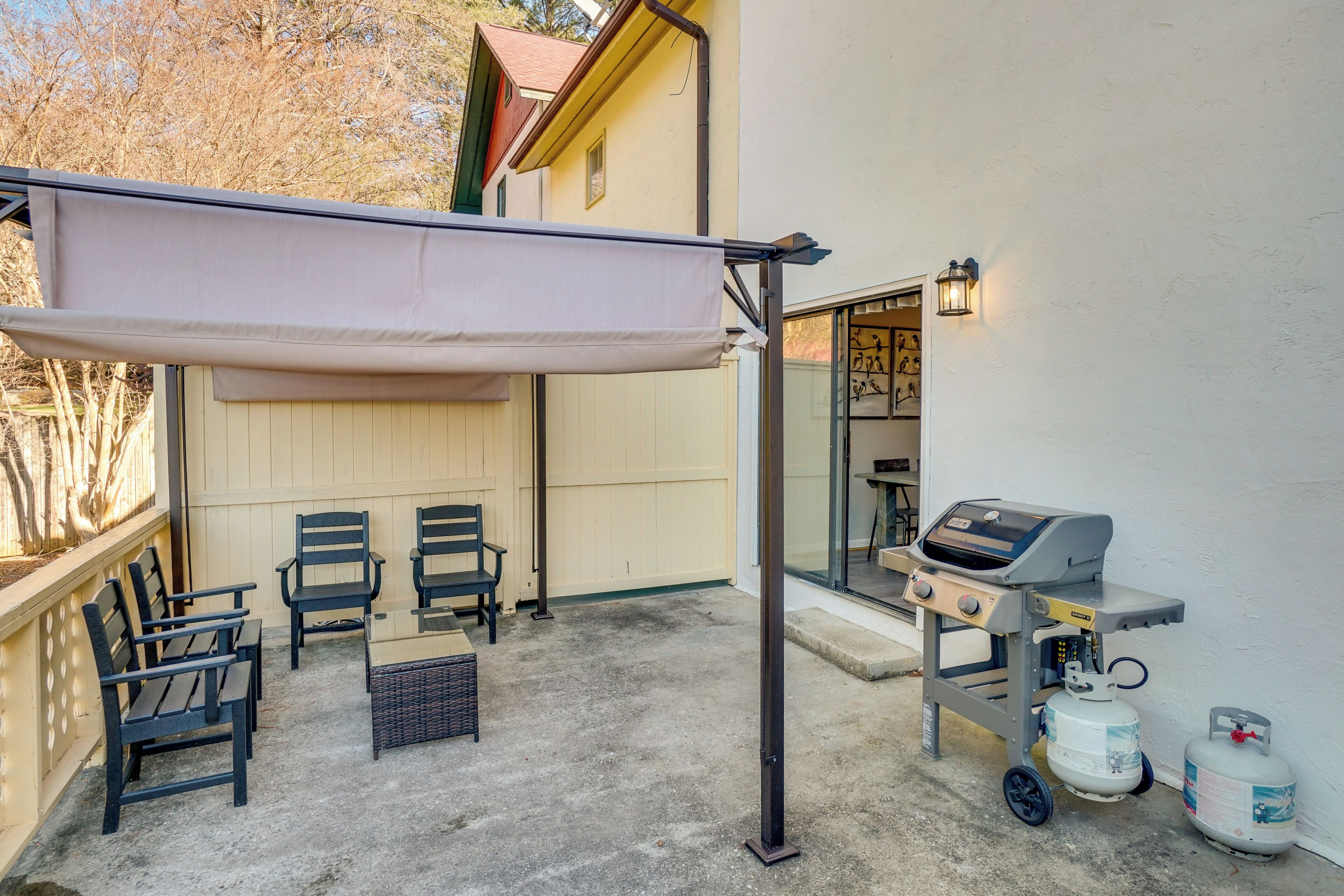 An outdoor patio with a grill, chairs, and a canopy.