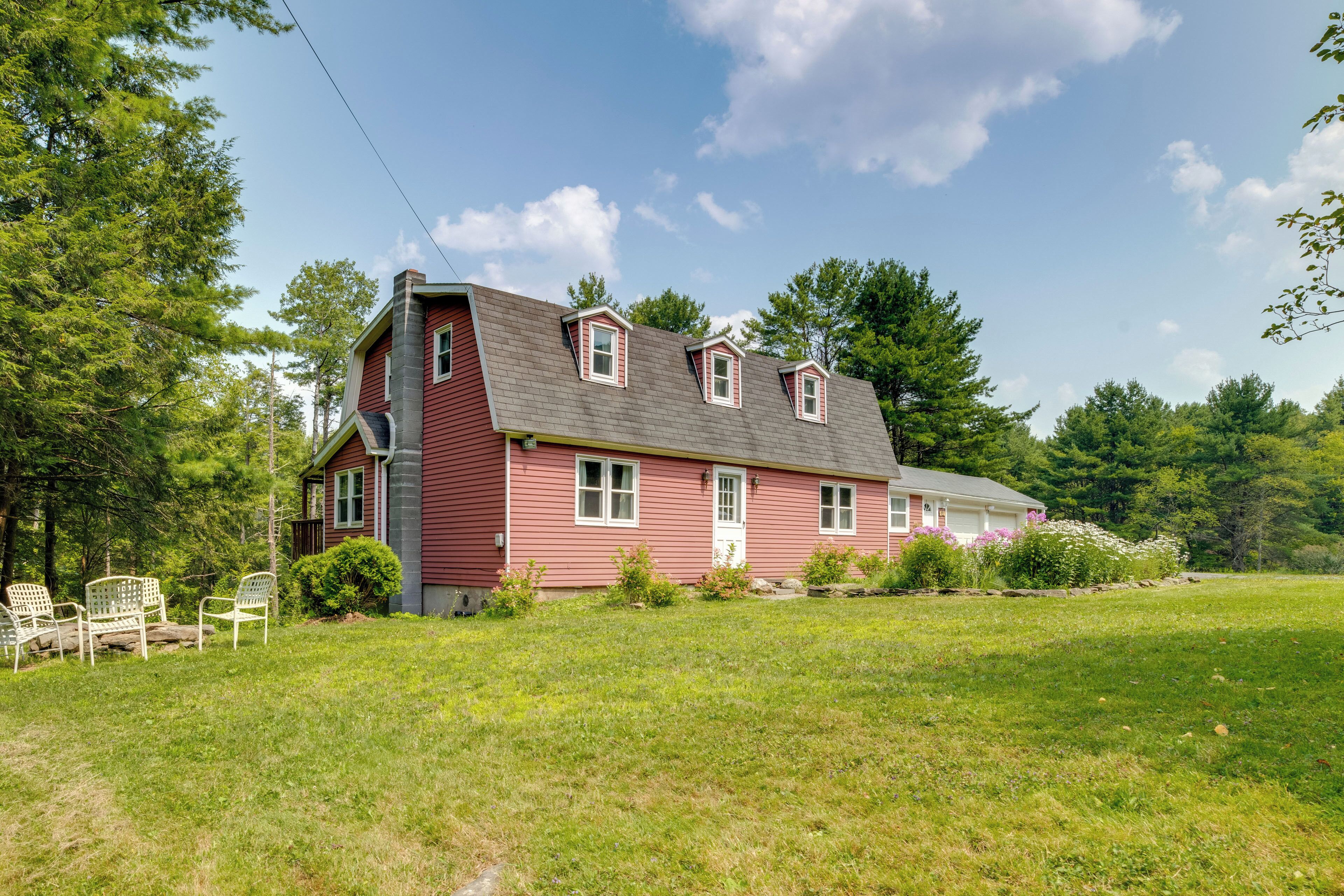 A red house with a sloped roof, a chimney, and a front porch with chairs.
