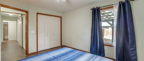 A bedroom with a bed, a ceiling fan, a window with curtains, and a door leading to a hallway.