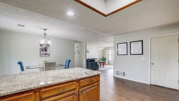 A spacious kitchen with a granite countertop, wooden cabinets, and a ceiling fan.