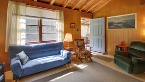 A cozy living room with a blue sofa, patterned armchair, and green armchair. A wooden ceiling and a framed painting are visible. - 'the Acres' Panther Pond Cabin w/ Beach & Dock! (Raymond)