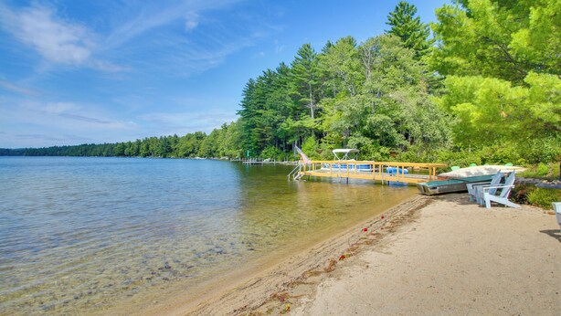 A lakeside area with a dock, boats, and a sandy beach. - 'the Acres' Panther Pond Cabin w/ Beach & Dock! (Raymond)