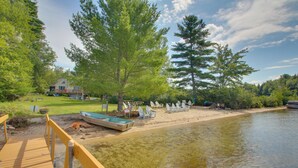 A lakeside deck with a boat, chairs, and a house in the background. - 'the Acres' Panther Pond Cabin w/ Beach & Dock! (Raymond)