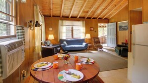 A cozy cabin interior with a dining table set for two, a blue sofa, and a kitchen area. - 'the Acres' Panther Pond Cabin w/ Beach & Dock! (Raymond)