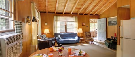 A cozy cabin interior with a dining table set for two, a blue sofa, and a kitchen area.